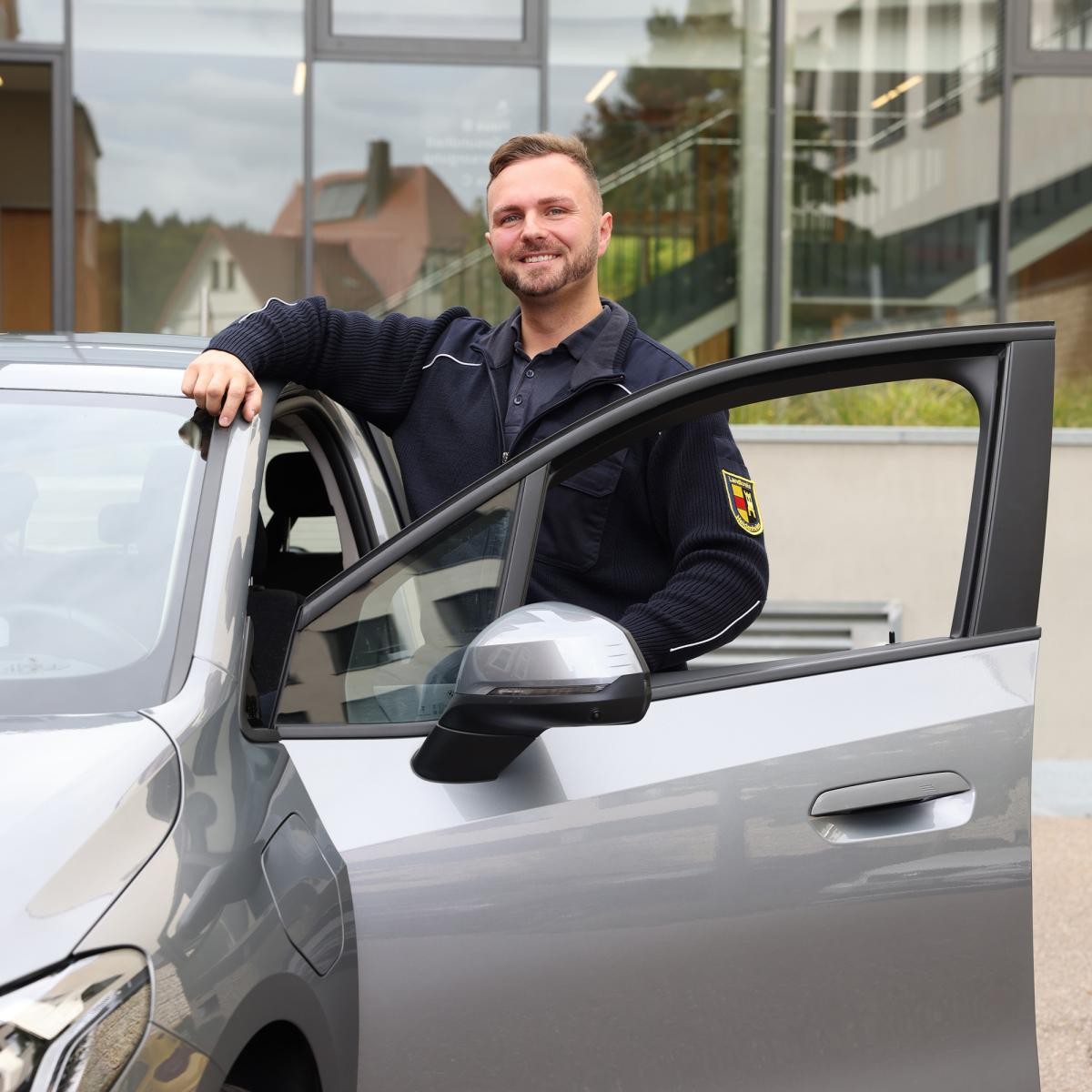 Mann mit Landkreis-Jacke steht neben einem Auto